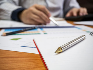Close up of pencil on notebook with businessman background