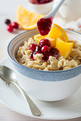  Oat porridge with cranberry sauce and orange in a ceramic bowl for healthy breakfast on a light background. Selective focus.