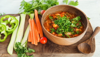Vegetarian soup in wooden bowl on wood board on white table