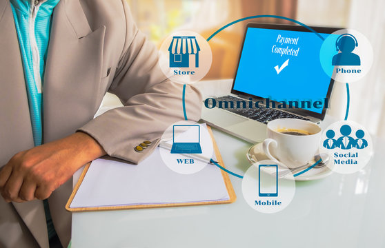 Marketing Data mangement platform and Omnichannel concept image. Omnichannel element icons on Business man place his hand on blank paper on the table and laptop computer with payment on screen.