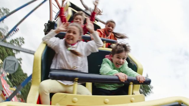 Joyful kids screaming and raising arms while riding roller coaster in amusement park