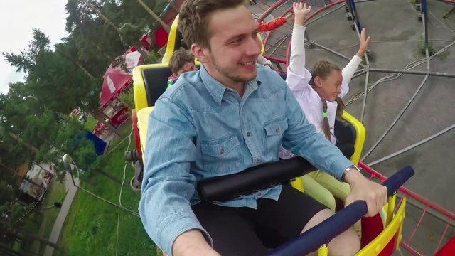 POV shot of man holding action camera while riding roller coaster with group of excited children in amusement park