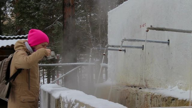 Young woman with a backpack drinks mineral water from hot springs in the resort of Arshan, Buryatia, Siberia, Russia