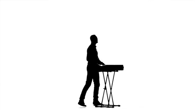 Man playing on a synthesizer. Jumps to the music. Silhouette