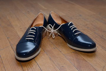 Closeup photo of patent-leather female shoes with laces on woode
