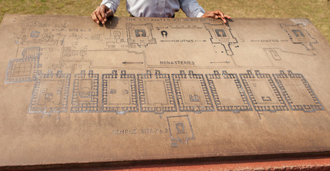 Archaeological heritage of India, ruins of university of Nalanda. Stone with the scheme of excavation. The hands of the Indian guide and plan of territory.