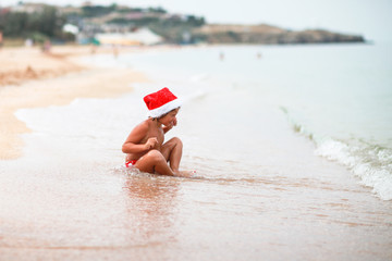 tanned Caucasian kid girl in santa hat on  beach with yellow san
