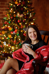 Young woman sits in a rocking-chair near Christmas-tree.