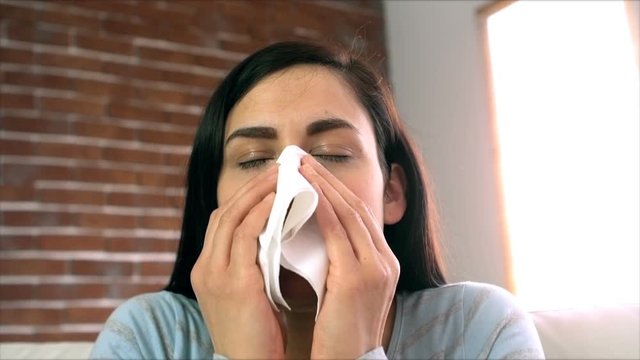 Woman blowing her nose on couch