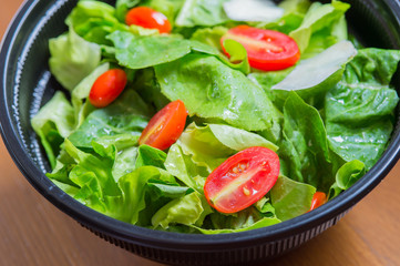 Organic mixed green salad in a transparent plastic plates on  wooden table very tasty