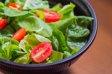 Organic mixed green salad in a transparent plastic plates on  wooden table very tasty