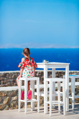 Adorable little girl having breakfast at outdoor cafe with sea view. Time for lunch.