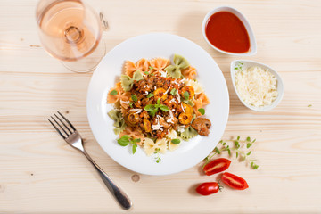 Italian pasta Farfalle with meat, olives, basil and mushrooms. Rose wine glass visible. Top view.