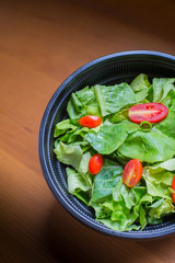 Organic mixed green salad in a transparent plastic plates on  wooden table very tasty