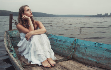 dreamy mysterious blonde girl in a white dress in an old boat on the lake