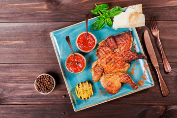 Roasted Chicken or turkey with spices, lemon, tomato sauce, basil and pita bread on plate on dark wooden background. Thanksgiving table served with knife and fork. Top view