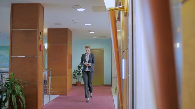 business lady goes along the corridor, holding in hand the tablet