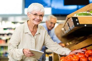 Smiling senior woman with list buying apple