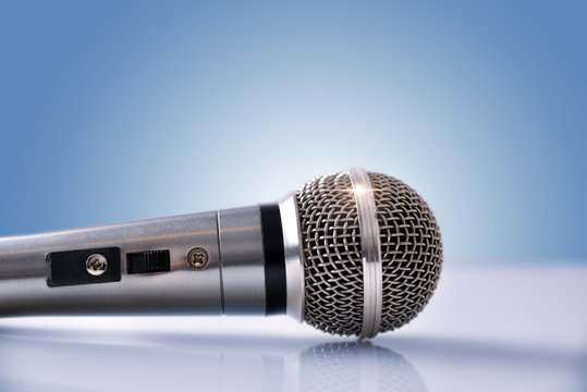 Microphone with reflections on white glass table and blue backgr