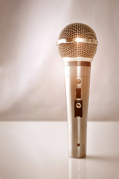 Microphone with golden reflections standing on a white glass