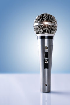 Microphone with reflections standing on white table and blue bac