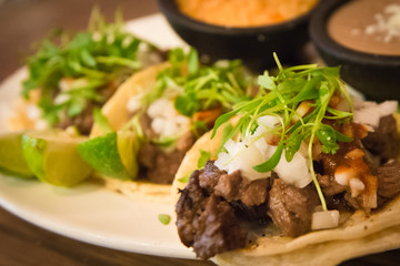 Plate of three street style tacos topped with micro greens, onions, chives and various sides