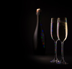 two glasses with champagne and bubbles on the background of the bottle, dark color background