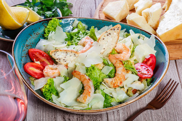 Shrimp salad with parmesan cheese, croutons, tomatoes, mixed greens, lettuce and glass of wine on wooden background. Healthy food. Top view