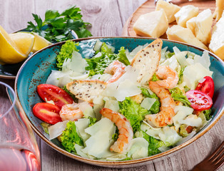 Shrimp salad with parmesan cheese, croutons, tomatoes, mixed greens, lettuce and glass of wine on wooden background. Healthy food. Top view