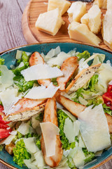 Salad with chicken breast, parmesan cheese, croutons, tomatoes, mixed greens, lettuce and glass of wine on light wooden background. Ingredients on table