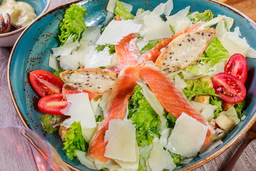 Salmon salad with tuna sauce, parmesan cheese, croutons, tomatoes, mixed greens, lettuce and glass of wine on wooden background. Mediterranean food. Top view