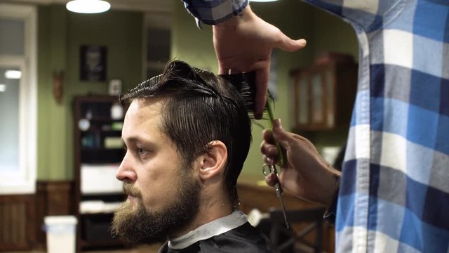 Barber making haircut of attractive bearded man in barbershop