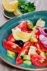 Greek salad of organic vegetables with tomatoes, cucumbers, red onion, olives, feta cheese and glass of wine on wooden background. Top view