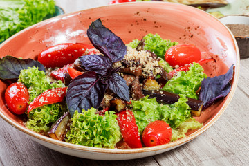Hot salad with grilled tomatoes, eggplant, zucchini, red pepper, salad leaves, garnished with grated walnuts and basil and glass of wine on wooden background. Italian food. Top view