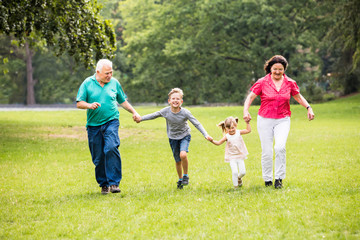 Fototapeta na wymiar Grandparents And Grandchildren Running In Park