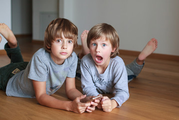 Two surprised kids lying on wooden floor and using mobile phone    © Tatiana Murr