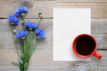 Blue cornflowers, blank paper and coffee cup top view