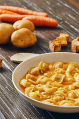 Tortellini soup in white dish on wooden table