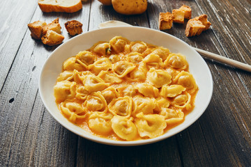 Tortellini soup in white dish on wooden table