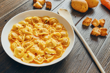Tortellini soup in white dish on wooden table