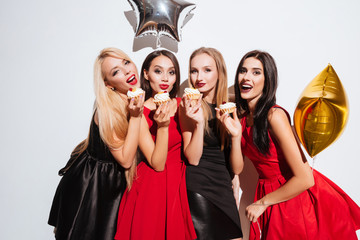 Four happy women standing and eating cupcakes on the party