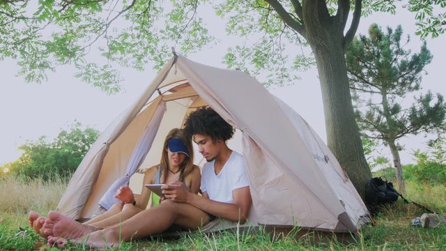 Camping couple in tent using tablet looking at photos