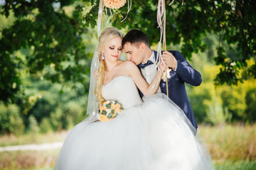 Wedding day. Married, cute couple near the swing after wedding ceremony. Beautiful bride with bouquet of flowers and elegant groom walking after wedding ceremony.