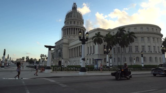 Old rare retro cars and bicycle taxi are riding near the ancient colonial Capitol building in a central empty crossroad of Havana city at sunset evening time