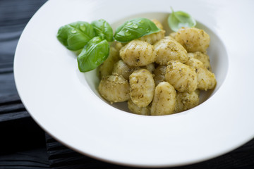 Close-up of a glass white plate with gnocchi and basil pesto