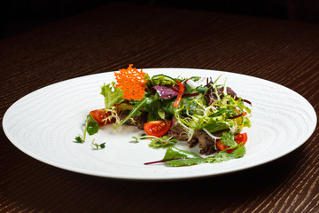 Vegetable salad menu for the restaurant in a large white plate on a white table cloth on a wooden table. Salad on the table with knife and fork. Svezhive vegetables.