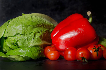raw lettuce, red peppers and tomatoes on black background