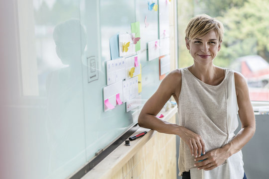 Smiling businesswoman with adhesive notes at whiteboard in modern office