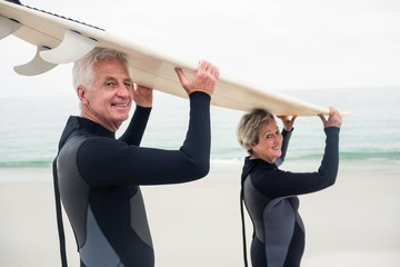 Senior couple in wetsuit carrying surfboard 