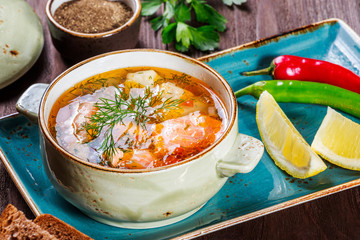 Fish soup with salmon and shrimps, dill, potatoes, lemon, peppers and bread on dark wooden...